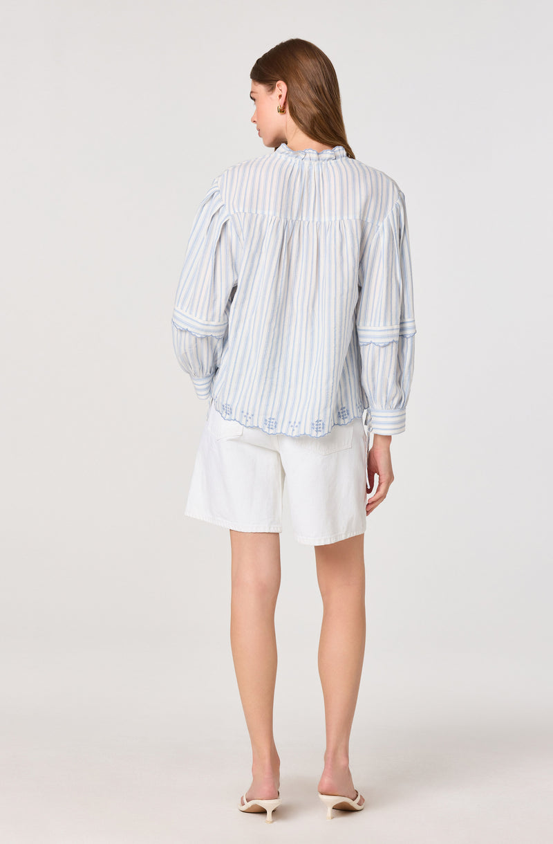 Woman wearing a light blue and white striped long-sleeve blouse and white shorts.