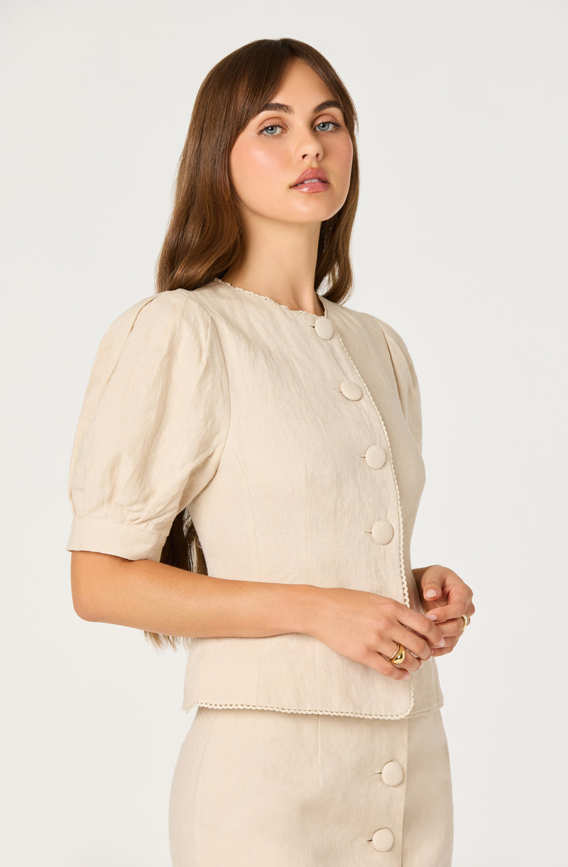 Woman in beige puff-sleeve blazer and matching skirt with large buttons.