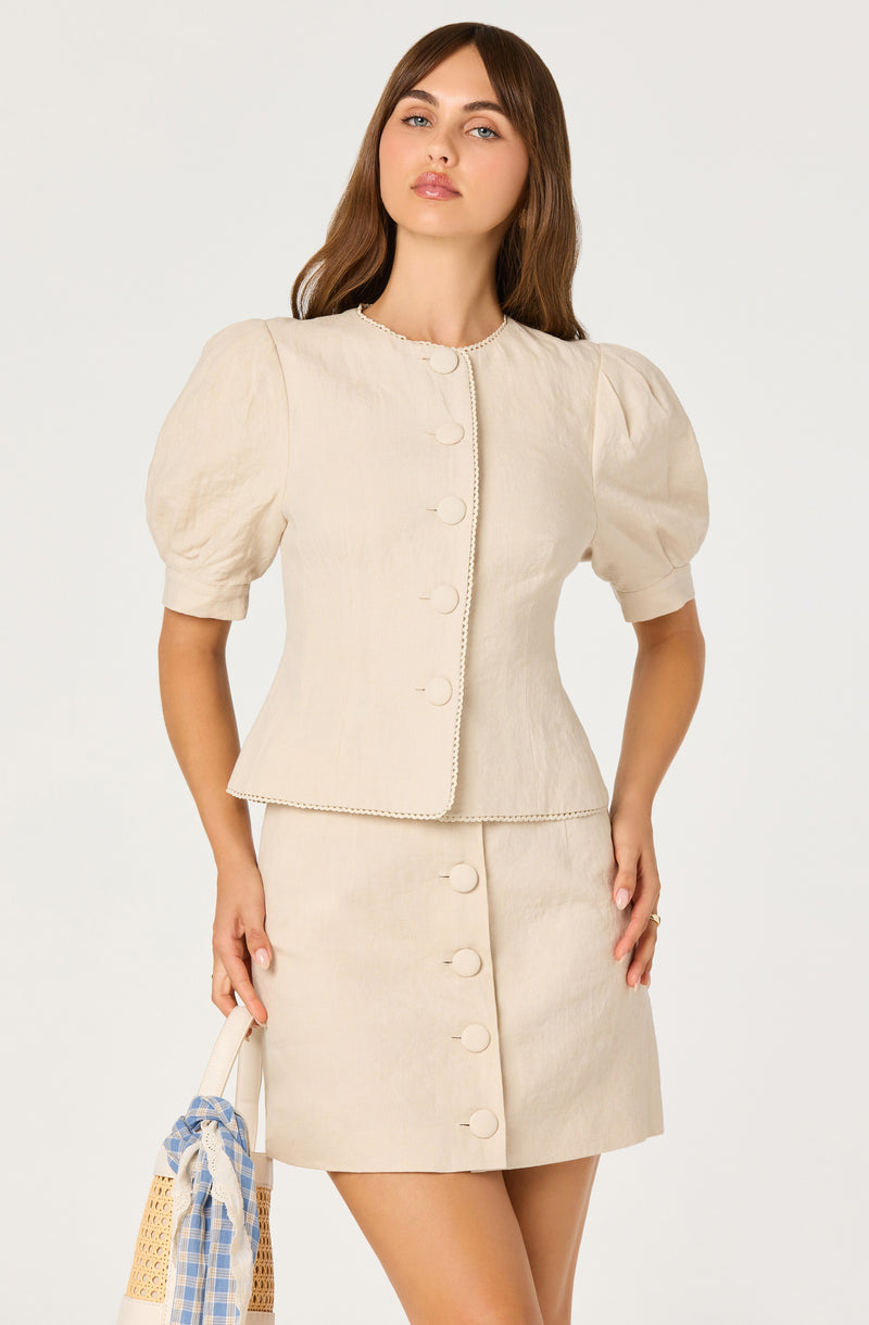 Woman wearing a beige top with puff sleeves and a matching skirt with large buttons.