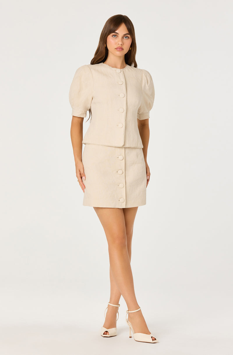 Beige two-piece outfit with puff sleeves and large buttons, paired with white high heels.
