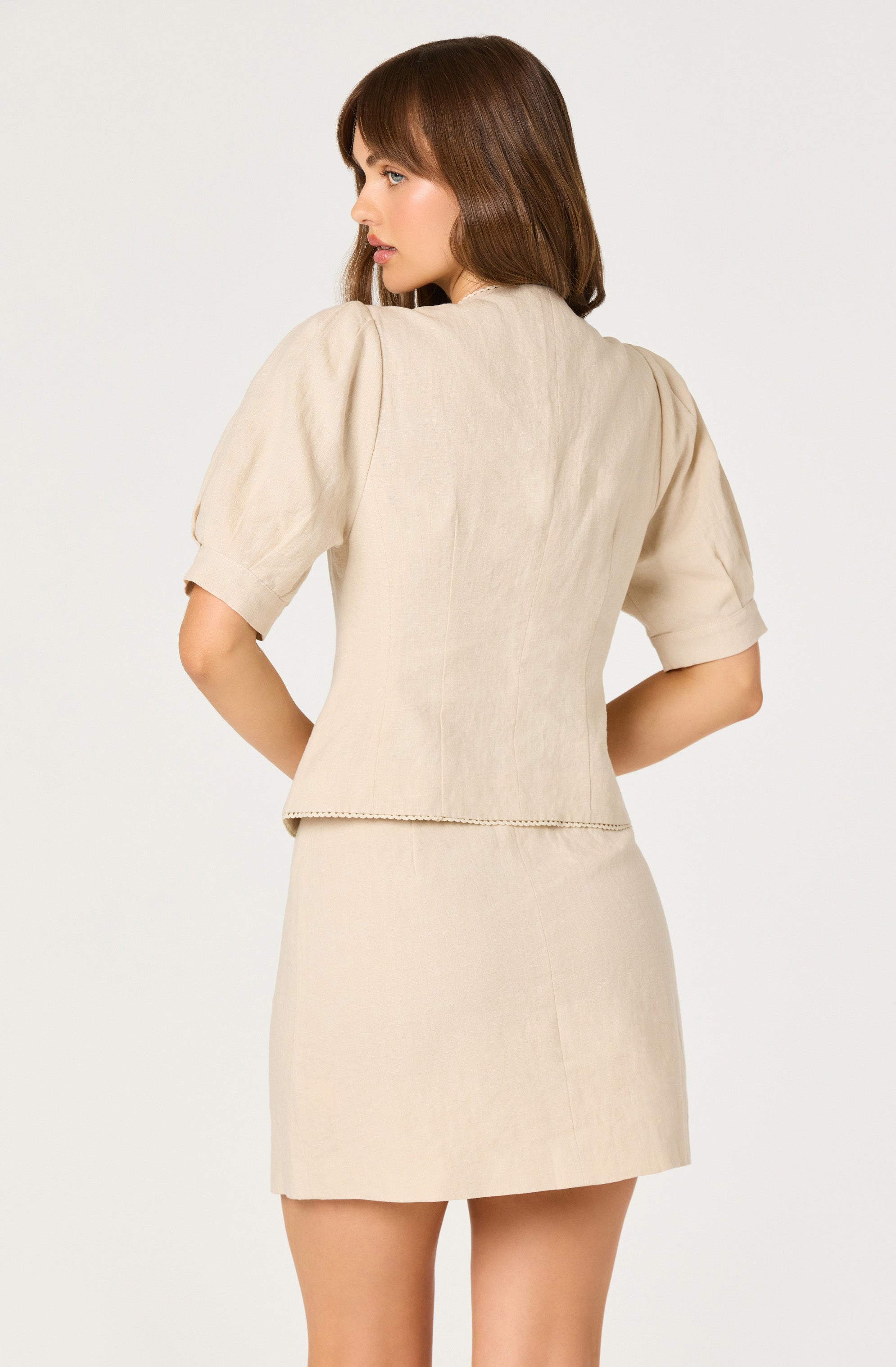 Woman in beige short-sleeve blouse with puffed sleeves and matching beige skirt.