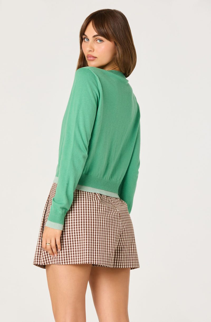 Woman wearing a green sweater and a brown checkered skirt.