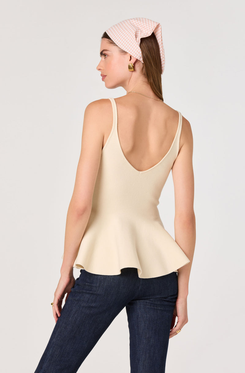 Woman wearing a sleeveless, cream-colored top with a peplum hem and thin shoulder straps.