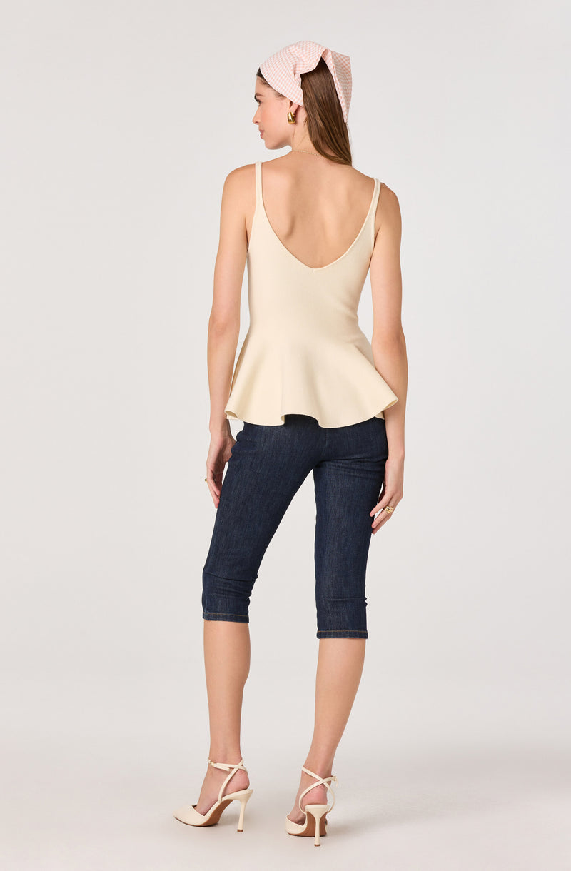 Woman wearing a cream sleeveless top with a peplum hem, dark denim capri jeans, beige high heels, and a pink headscarf.