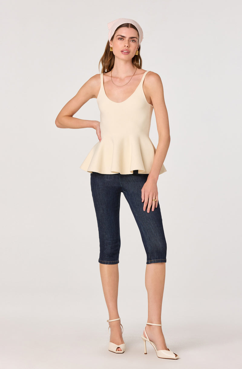 Woman wearing a cream peplum top, dark capri jeans, beige high heels, and a pink headscarf.