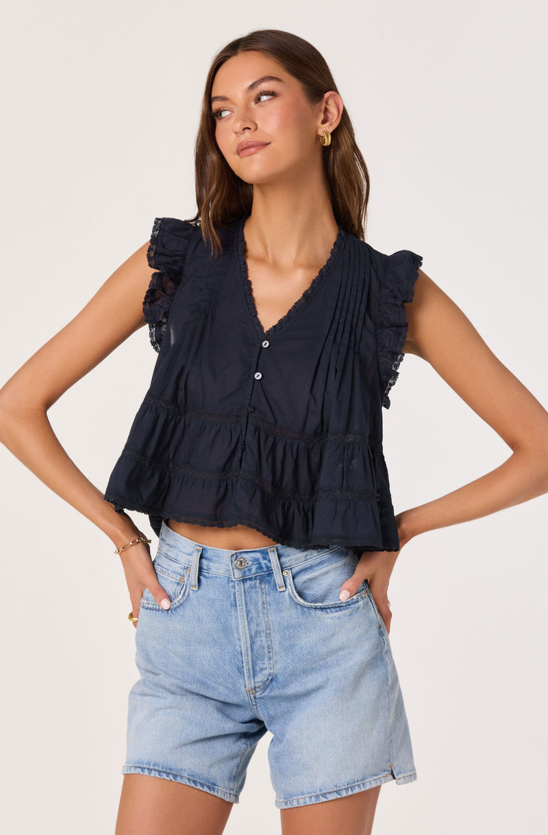 Woman wearing a navy sleeveless blouse with ruffled shoulder details and lace trim, paired with light denim shorts.