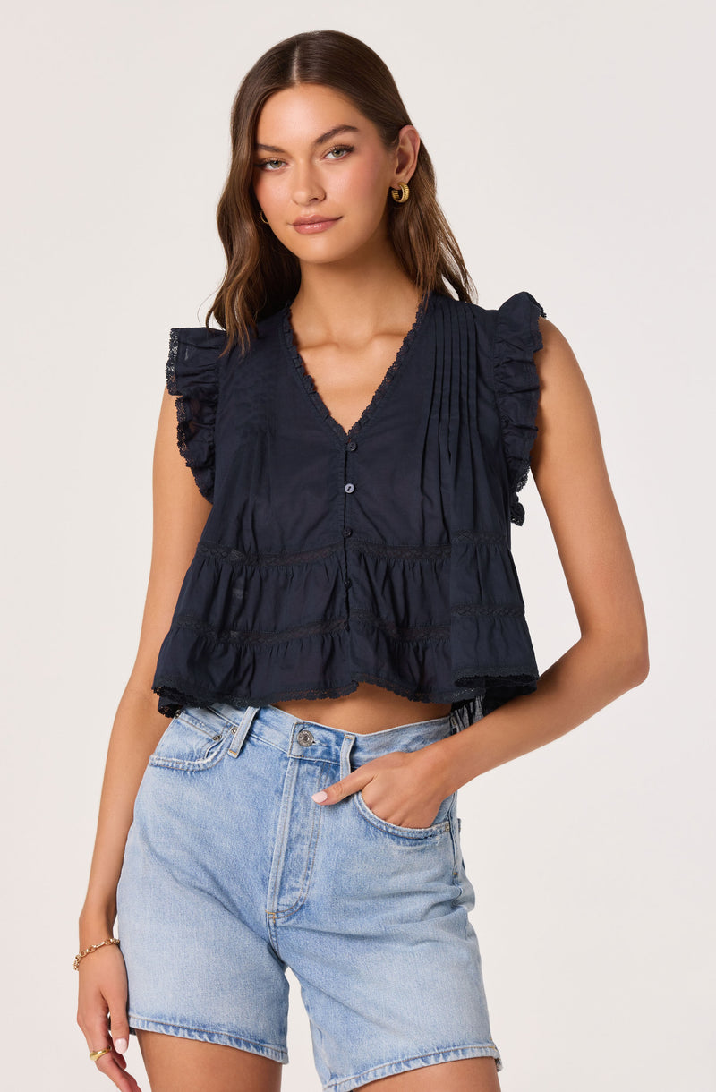 Woman wearing a navy blue sleeveless blouse with ruffled shoulders and light blue denim shorts.