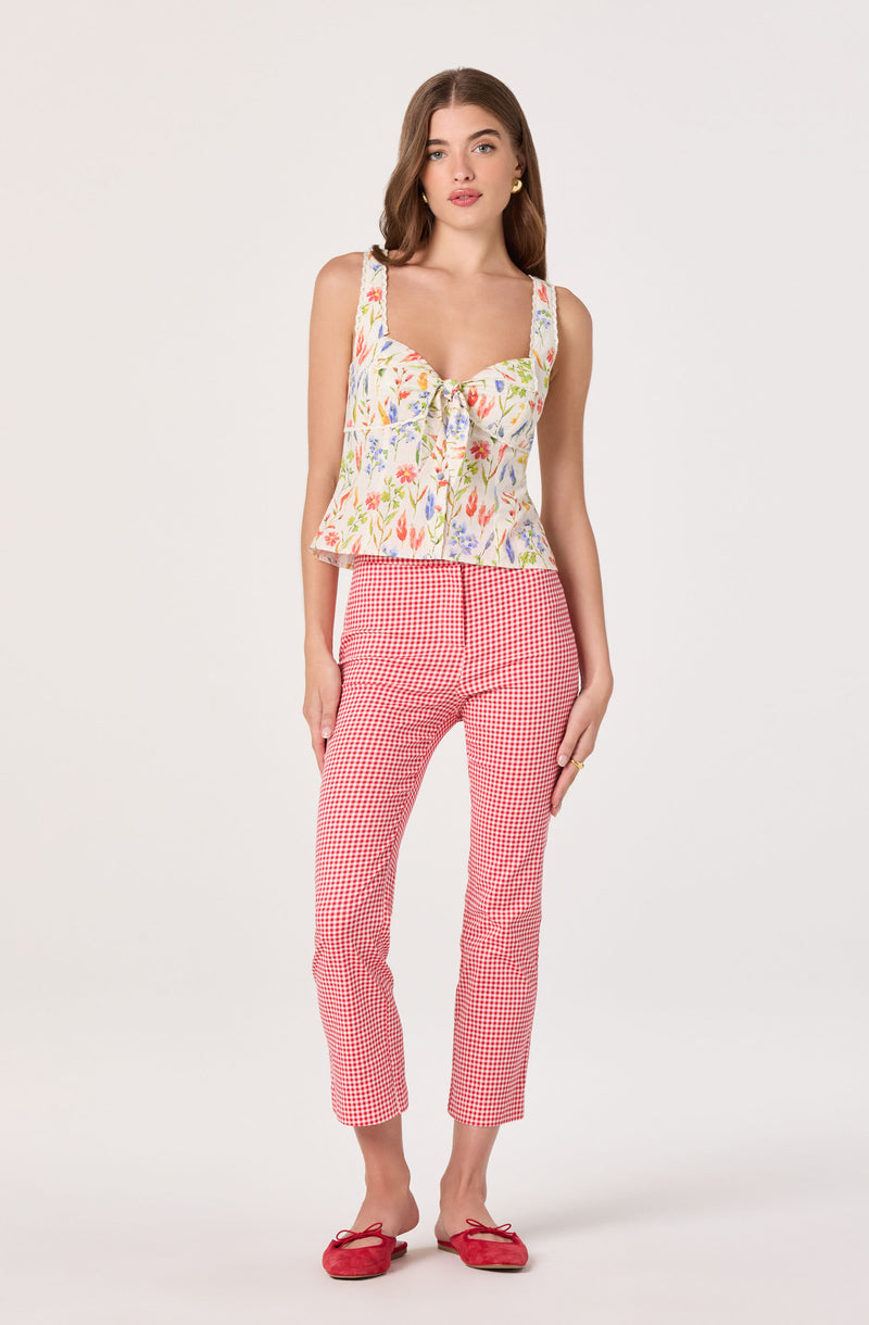 Woman wearing a sleeveless floral top, red and white checkered pants, and red flats.