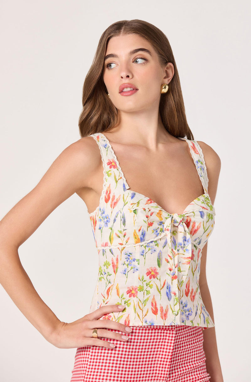 Woman wearing a floral sleeveless top with ruffled straps and red gingham shorts.