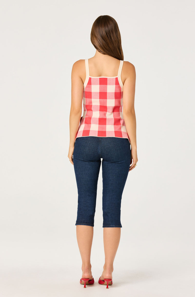 Woman wearing a pink and white checkered tank top and dark blue cropped jeans.