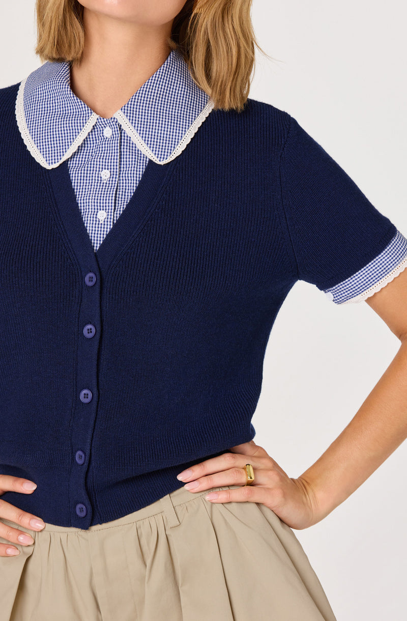 Woman wearing a blue cardigan over a blue and white checkered shirt with a collar.