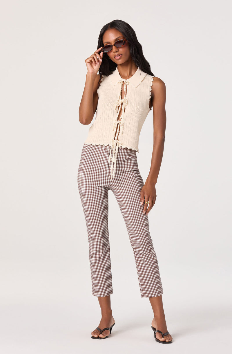 Woman in sleeveless cream knit top with tie-front, checkered pants, and sunglasses.