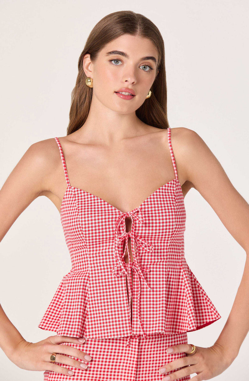 Woman in a red and white checkered sleeveless top with ruffle hem and front tie.