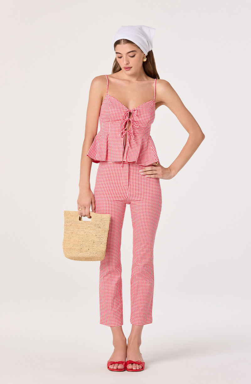 Girl wearing a red and white checkered sleeveless top and matching pants, holding a straw bag.