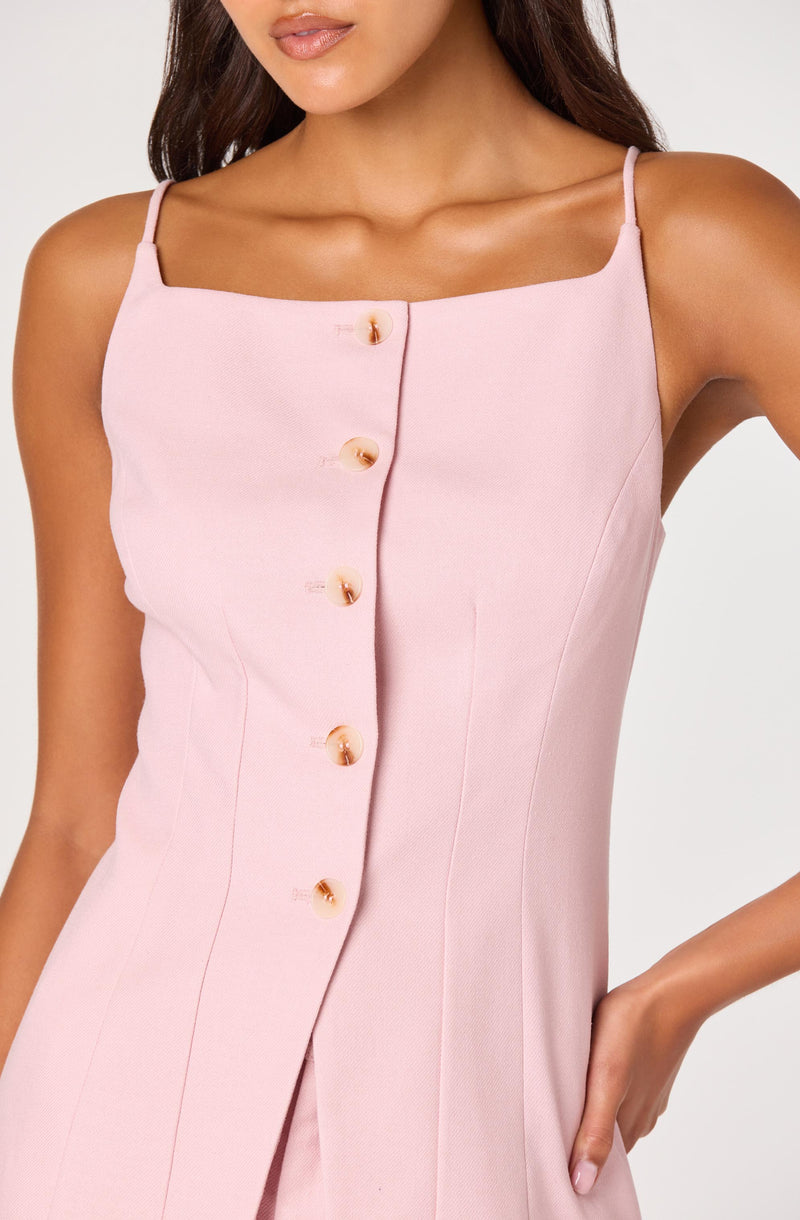 Woman wearing a light pink sleeveless dress with thin straps and button-down front.
