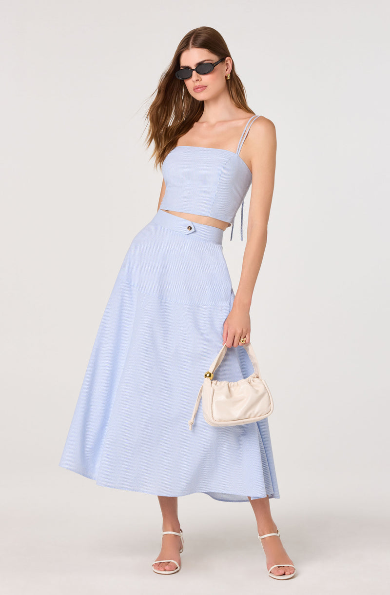 Woman wears a light blue crop top with spaghetti straps and a matching high-waisted, full-length skirt.