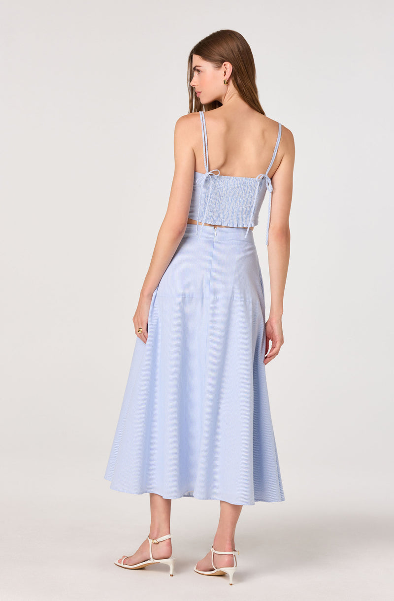 Woman wearing a light blue sleeveless crop top with tie straps and a matching long skirt.