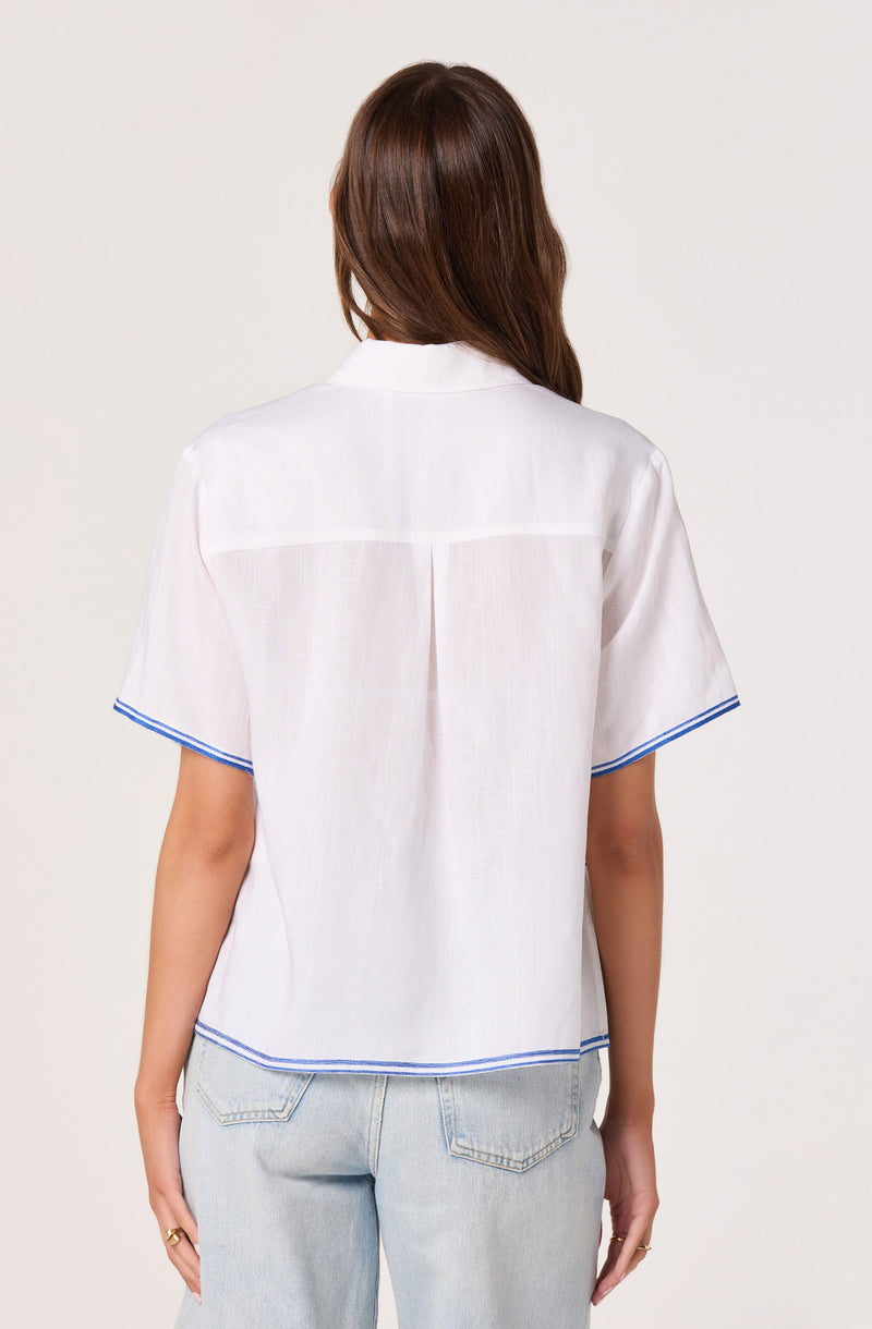 Woman wearing a white short-sleeve shirt with blue trim, and light-wash jeans.