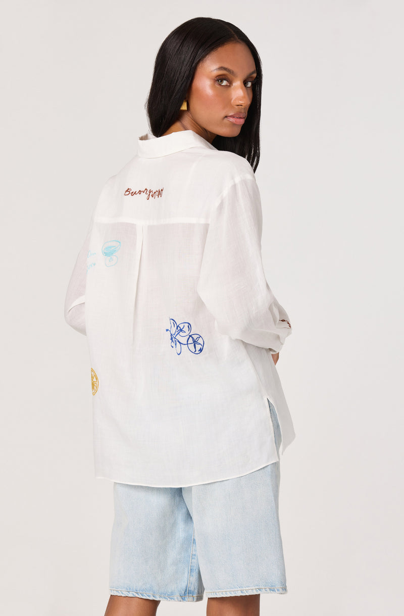 White shirt with colorful embroidered designs, paired with light blue denim shorts.