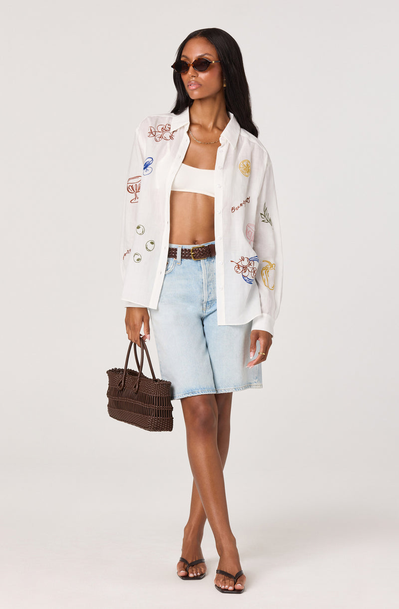 Woman wearing a white embroidered shirt, white crop top, light denim skirt, and black sandals.