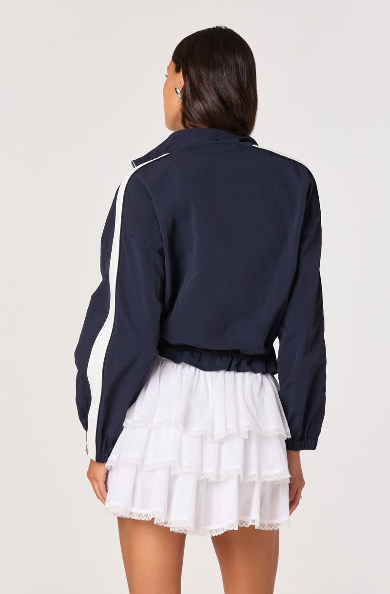 Woman in a navy jacket with white stripe on sleeve, paired with a white tiered ruffle skirt.