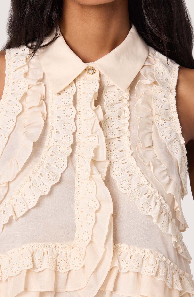 Cream sleeveless blouse with ruffled eyelet lace details and a pointed collar.