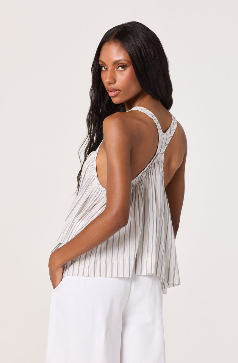 Woman wearing a sleeveless, striped, flowy top with white pants.