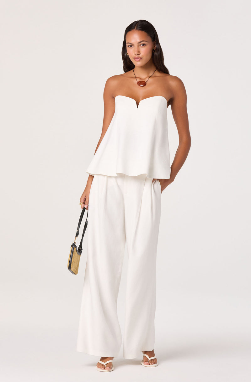 Woman wearing a strapless white top with a deep V neckline and wide-leg white pants.