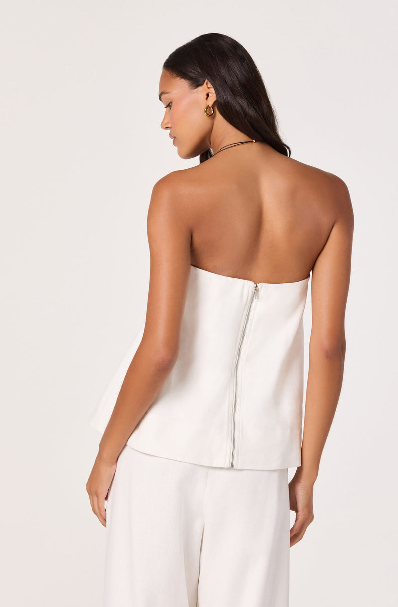 Back view of a woman in a strapless white top with a zipper, paired with wide white pants.