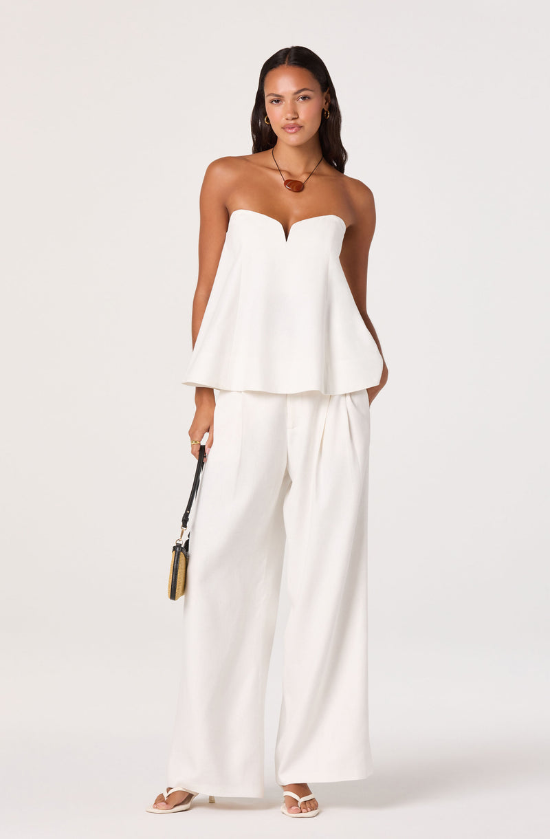 Woman wearing a strapless white top with wide-leg white pants.