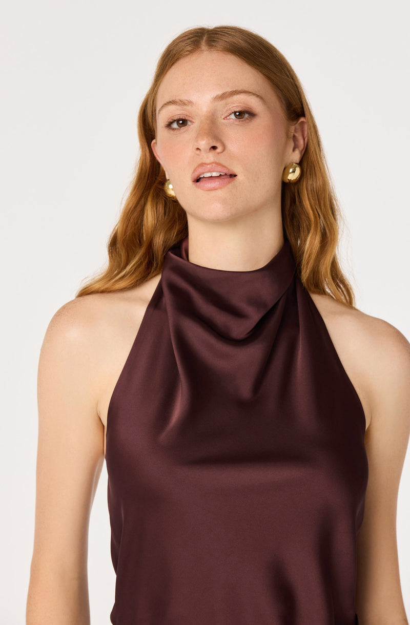 Woman wearing a sleeveless, satin burgundy top with a high neckline.