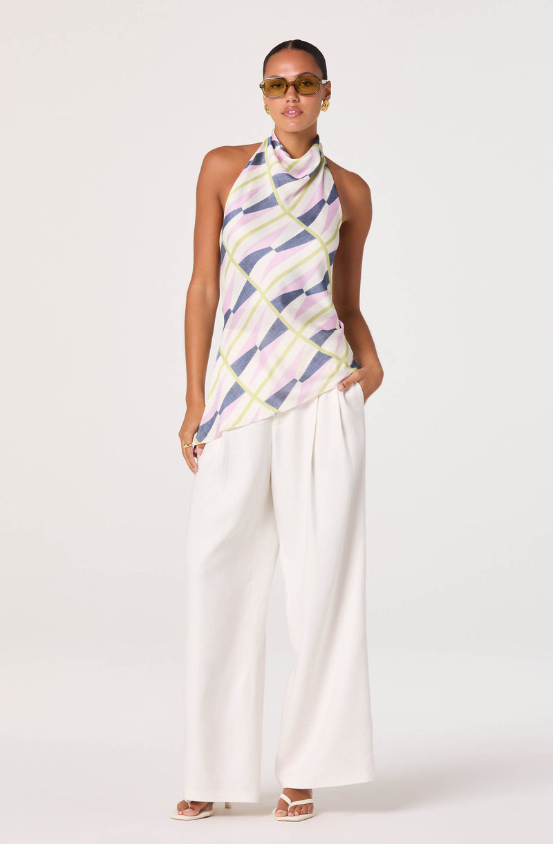 Woman wearing a sleeveless, patterned top with pastel colors and wide-leg white trousers.