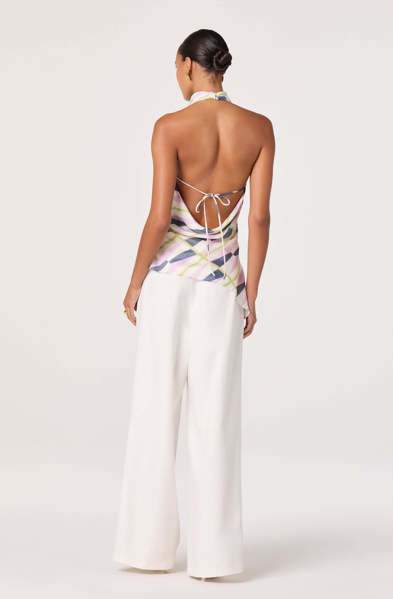 Back view of a woman wearing a colorful halter top with an open back and white wide-leg pants.
