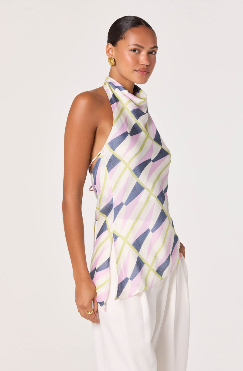 Woman wearing a colorful, geometric-patterned sleeveless top with a high neckline, paired with white pants.