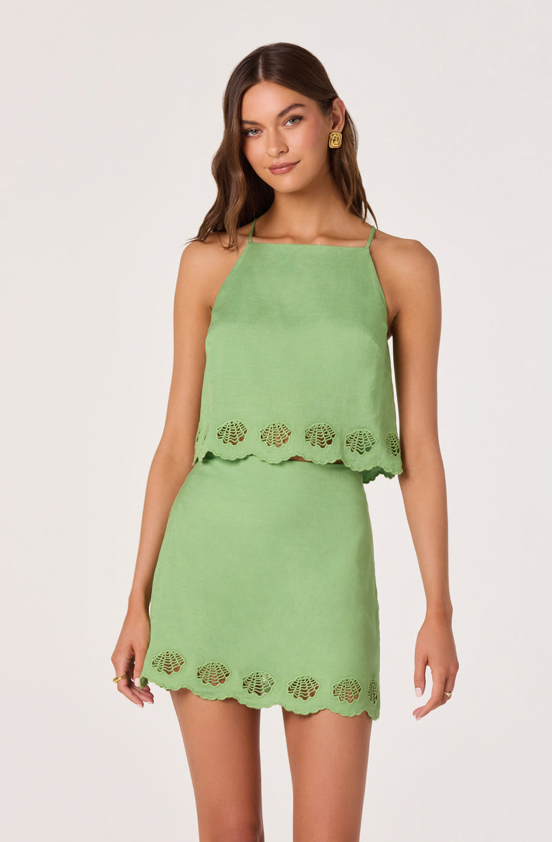 Young woman wearing a light green sleeveless top and matching skirt with scalloped edges and shell cutout details.