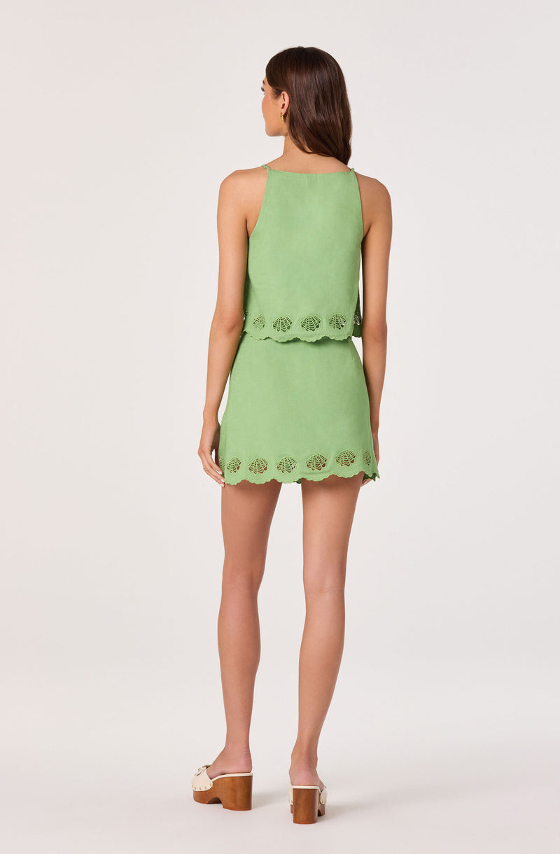 Woman wearing a green sleeveless top and matching skirt with scalloped edges and cut-out details.