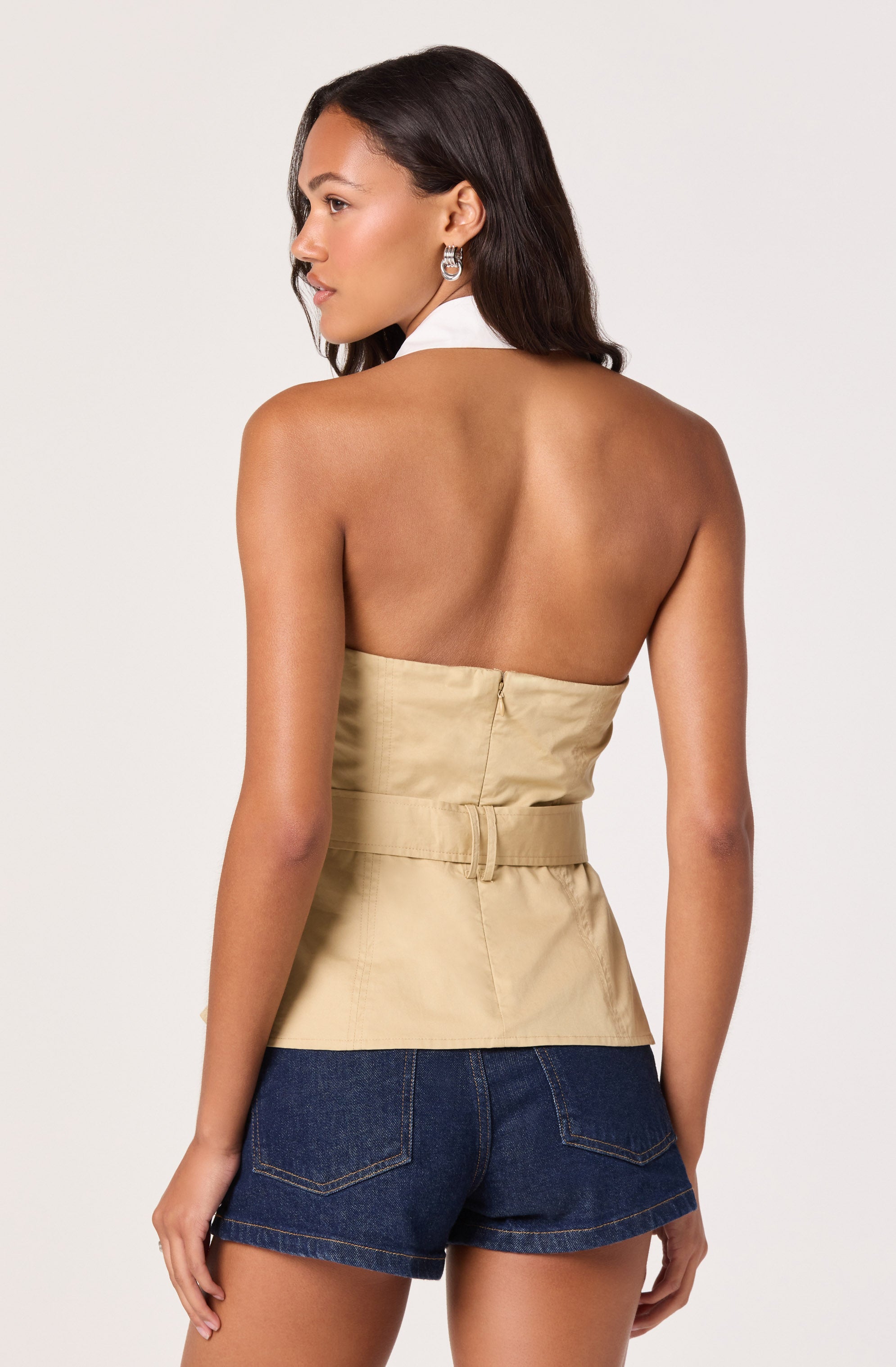Woman in a beige strapless top and dark denim shorts, facing away.