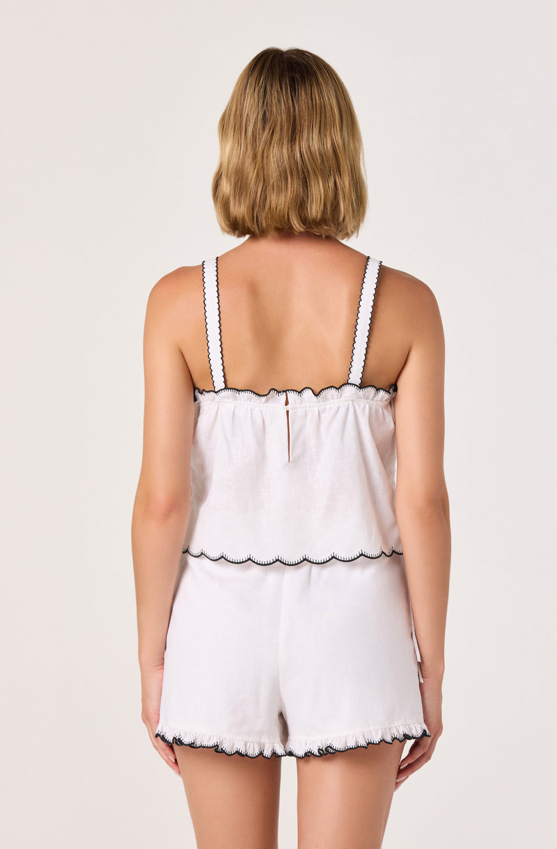 Woman in white sleeveless top and shorts with scalloped black trim, back view.