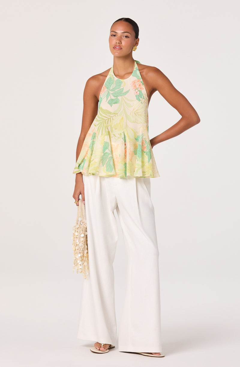 Woman wearing a sleeveless, halter-neck top with a pastel floral pattern and wide-leg white pants.
