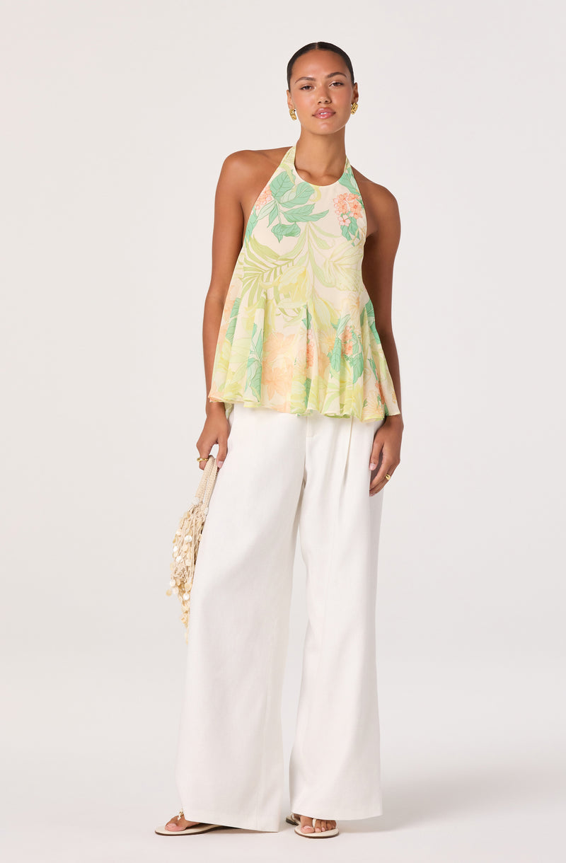 Woman wearing a colorful halter top with green and peach floral patterns and white wide-leg pants.