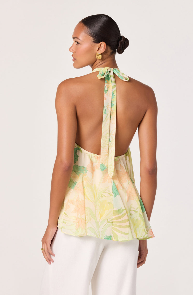 Back view of a woman wearing a sleeveless, halter-top dress with a pastel floral pattern and a bow tie around the neck.