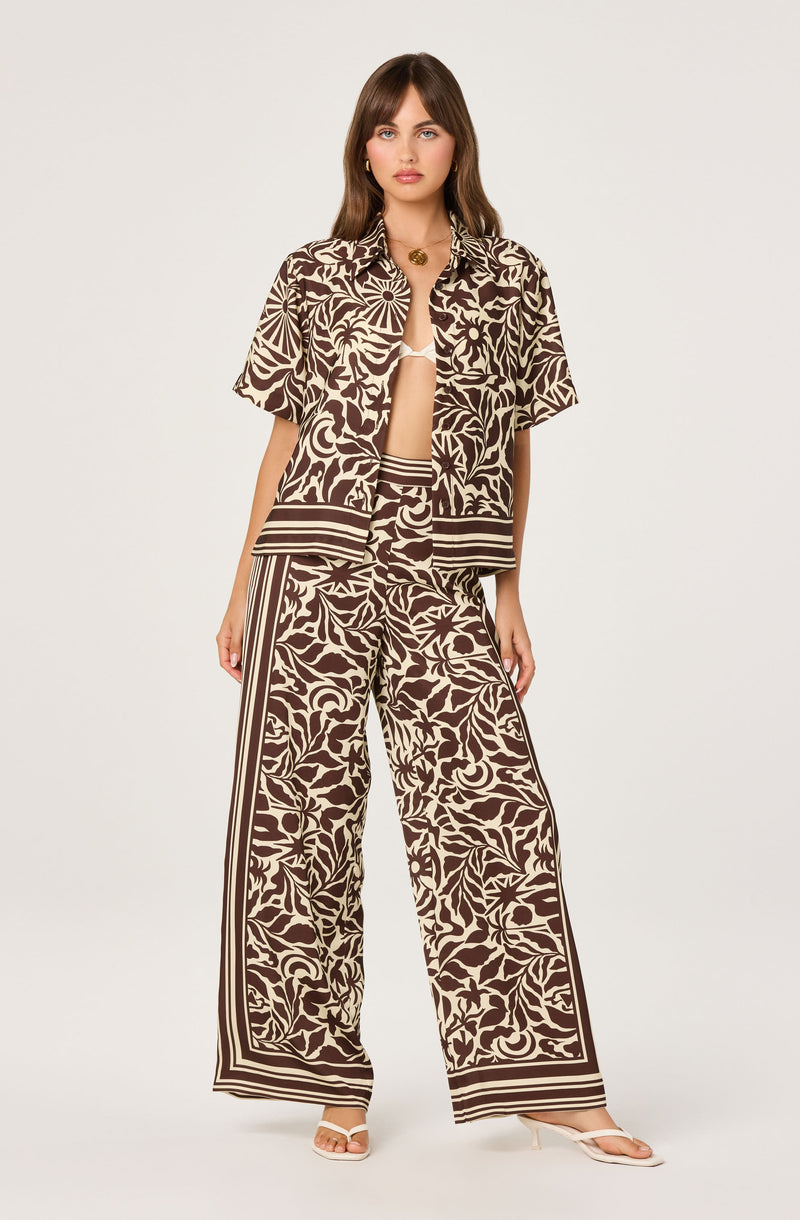 Woman wearing a brown and cream patterned short-sleeve shirt and wide-leg pants.