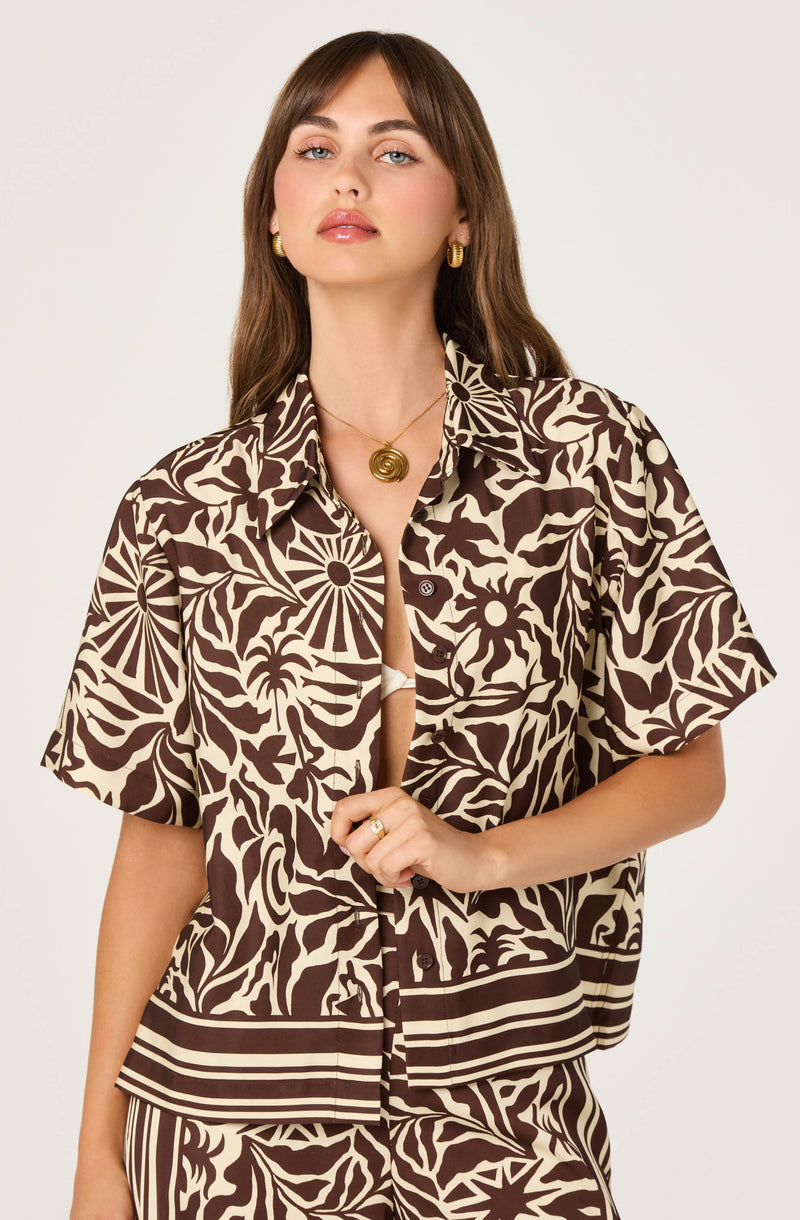 Woman wearing a short-sleeved, button-up shirt and matching pants with a brown and beige abstract leafy pattern.
