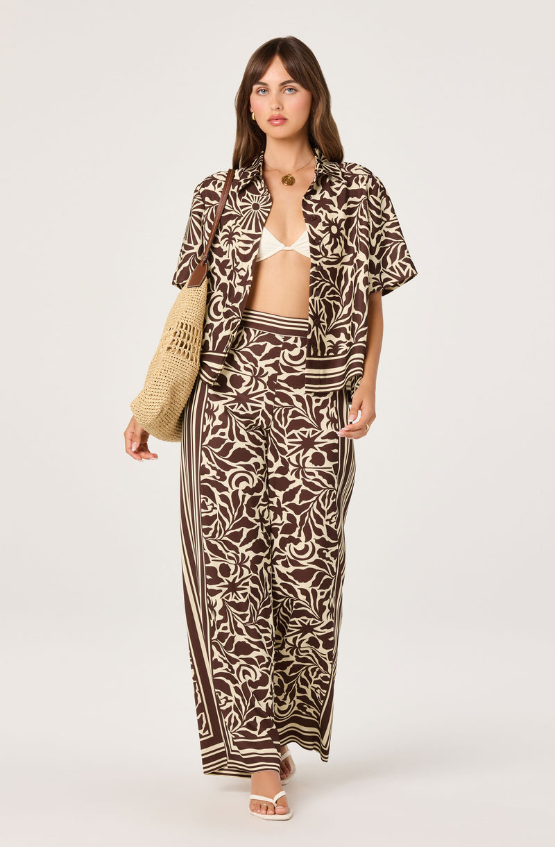 Woman wearing a brown and cream floral and striped matching outfit with a short-sleeve button-up shirt and wide-leg pants.