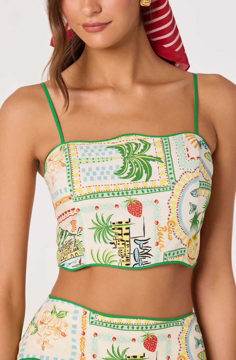 Woman wearing a colorful, tropical-themed crop top with green spaghetti straps.