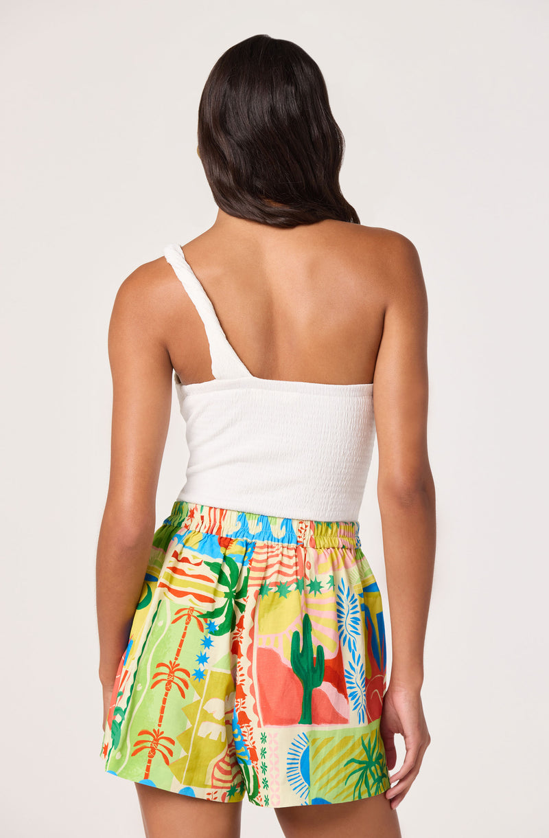 Woman wearing a white one-shoulder top and colorful tropical-print shorts.