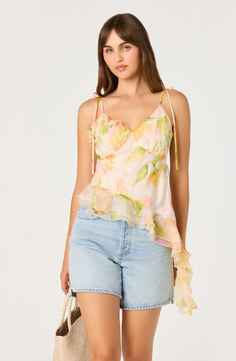 Woman wears a pastel floral sleeveless top with ruffles and light blue denim shorts.