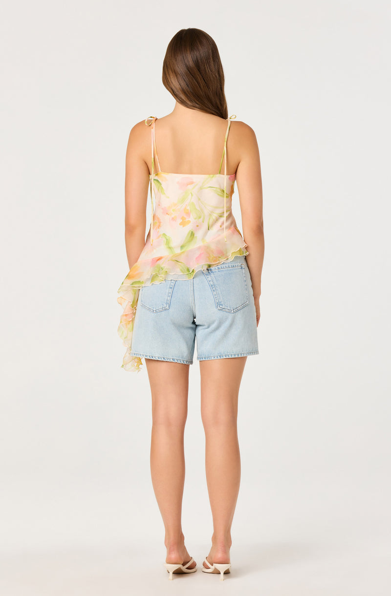 Woman wearing a pastel floral sleeveless top with ruffled hem, paired with light denim shorts.
