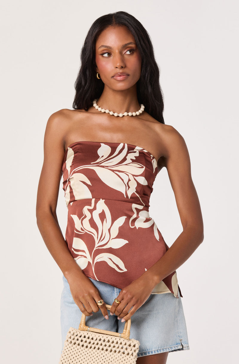 Woman wearing a strapless floral top in brown and cream, paired with light blue denim shorts.