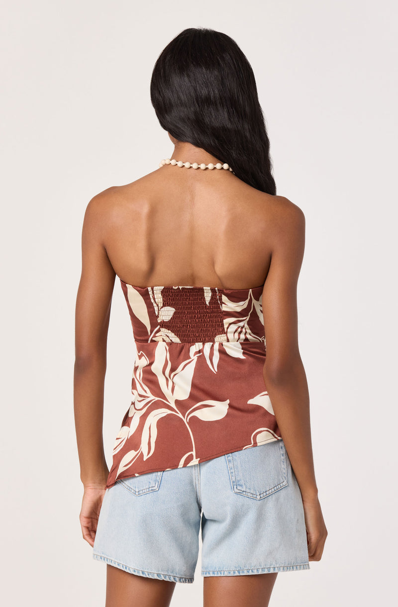 Back view of a woman wearing a strapless brown top with white floral print and light blue denim shorts.